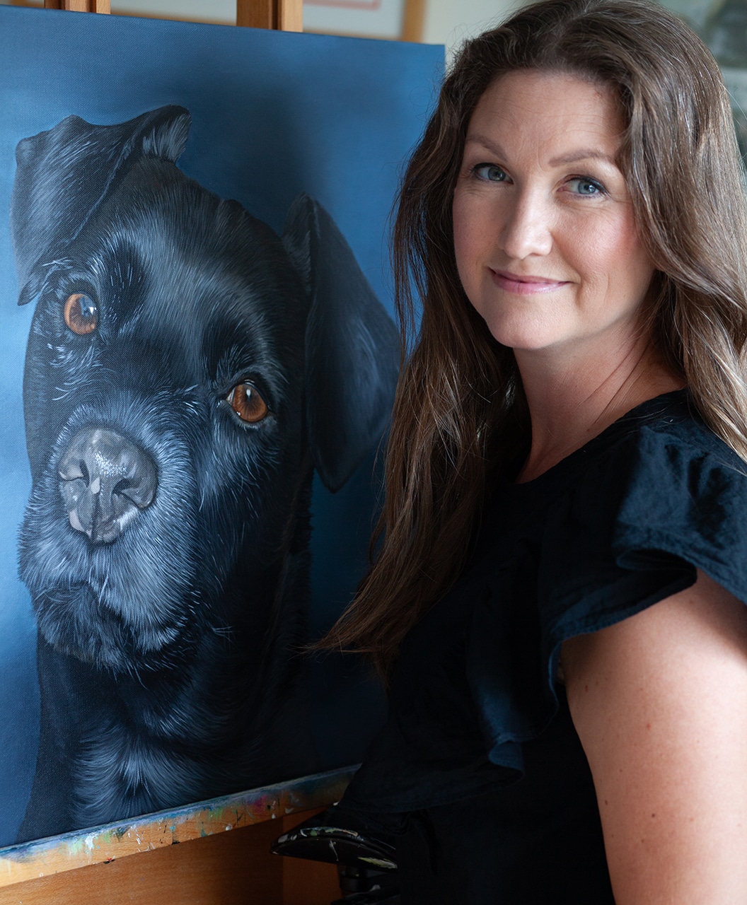 Artist, Erica Eriksdotter, next to one of her pet portraits, a black dog on canvas.