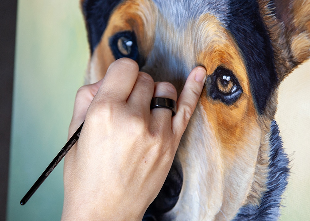 Close up of Erica Eriksdotter's hand wearing an Oura ring while painting a dog portrait